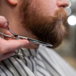 Man having his beard trimmed by a stylist with scissors